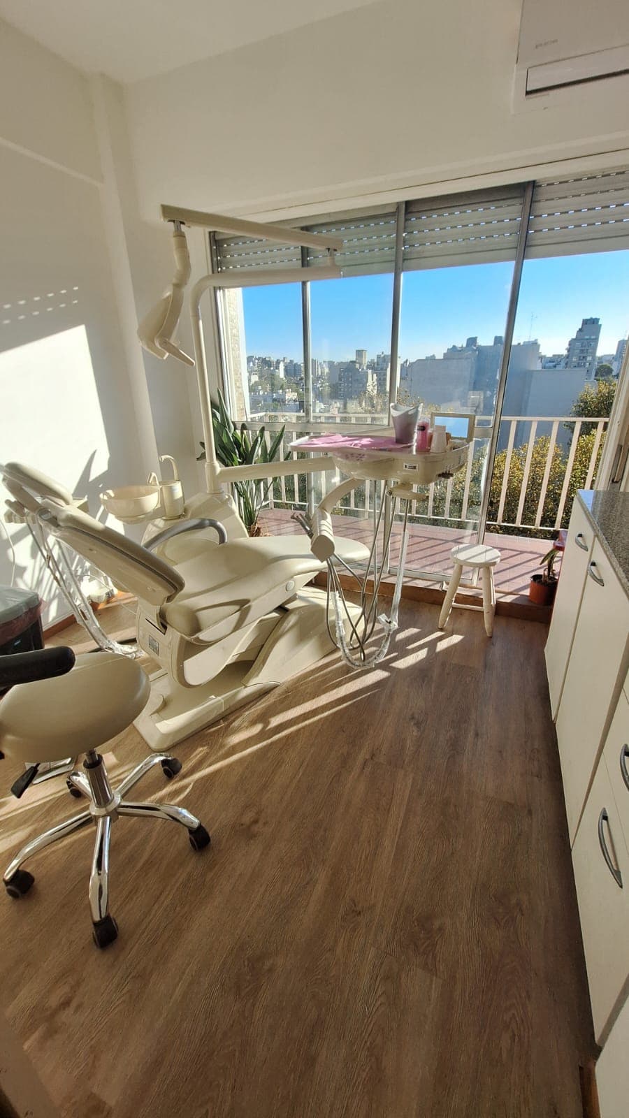 Sala de tratamiento con sillón dental moderno, luz natural y vista a la ciudad.